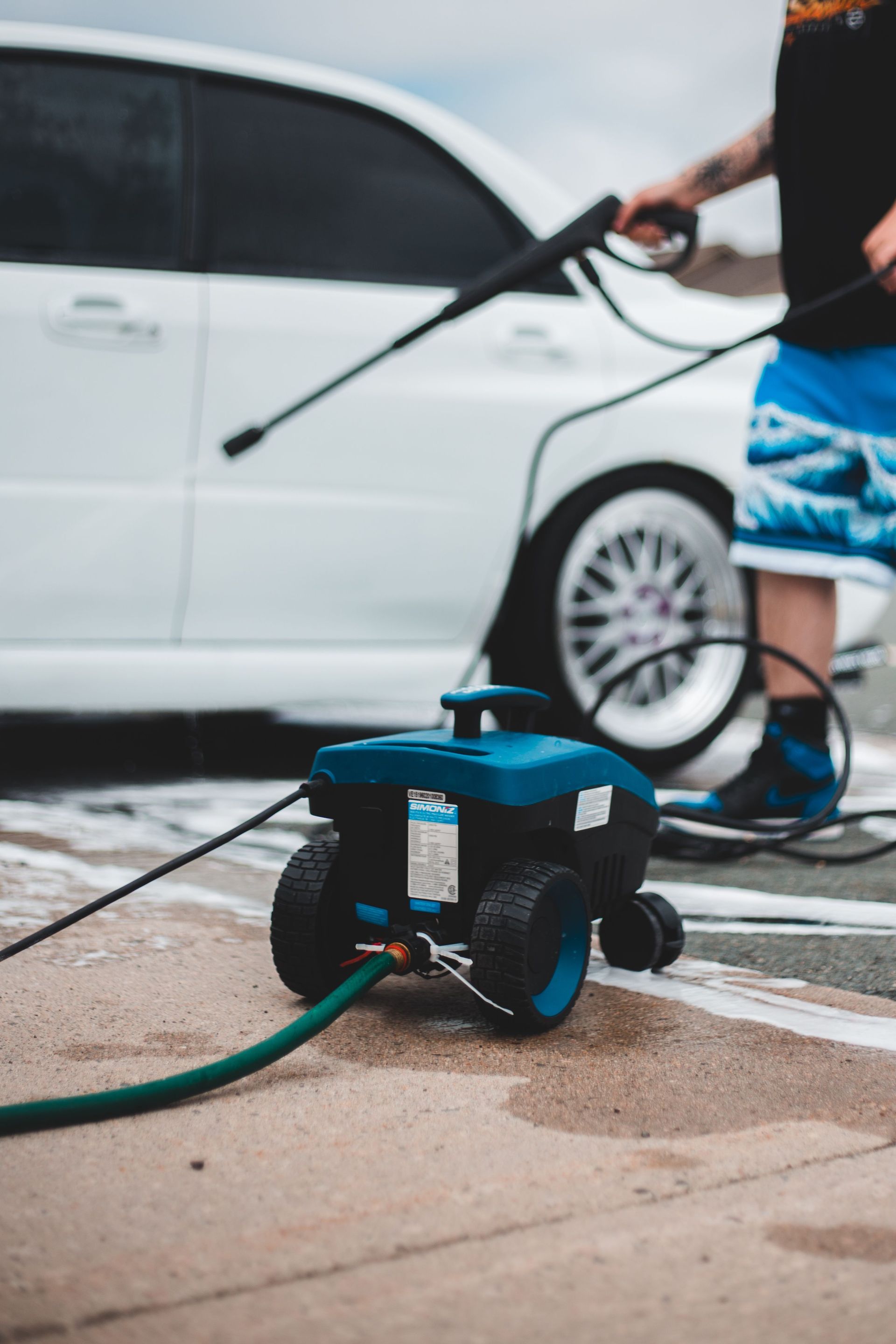 Power washer with hosepipe placed on pavement against car and crop person with pressure washer gun
